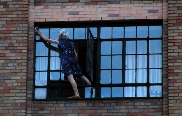Una abuela limpiando la ventana de su casa a fondo