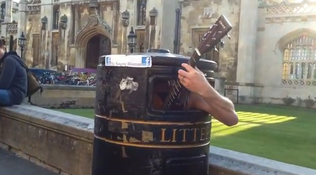 Un músico callejero canta y toca la guitarra dentro de una papelera