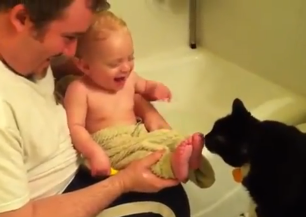 El bebé no puede aguantar la risa cuando el gato le lame los pies
