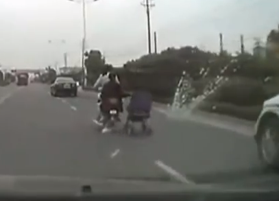 Una mujer china lleva un carrito de bebé de remolque en su moto