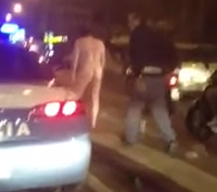 Un policía intenta meter en el coche a un hombre que camina desnudo por una calle de Nápoles