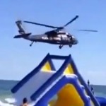 Un helicóptero volando bajo en la playa hace volar un tobogán hinchable con un niño dentro