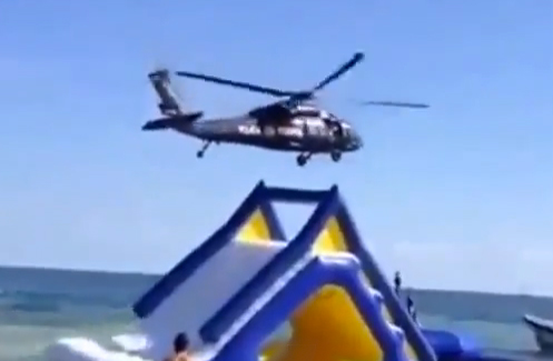 Un helicóptero volando bajo en la playa hace volar un tobogán hinchable con un niño dentro