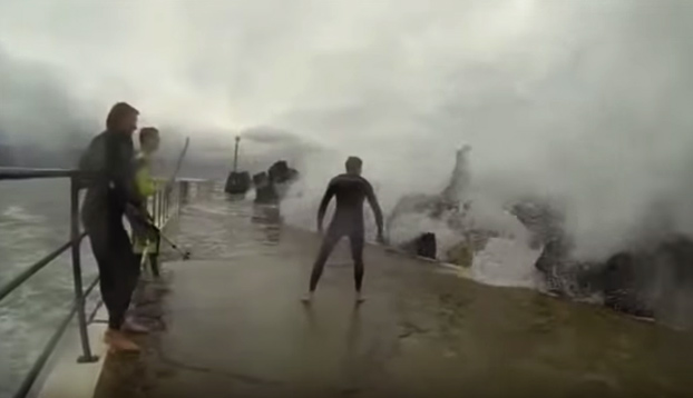 Varios amigos se colocan en un rompeolas para intentar aguantar los golpes de las olas