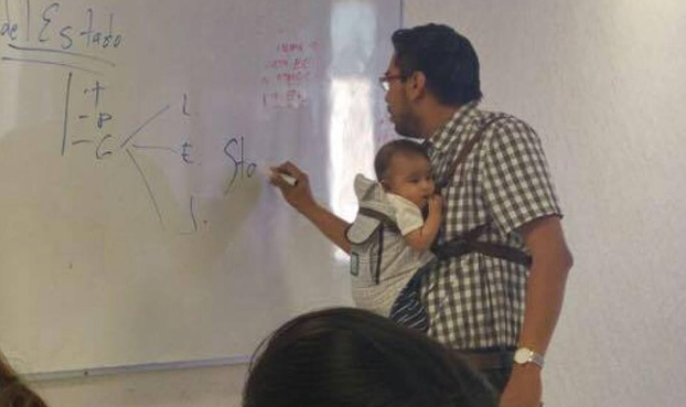 Un profesor universitario da clase con el bebé de una alumna en brazos