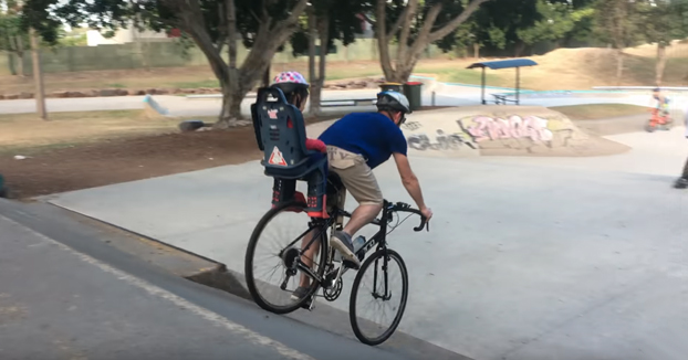 Padre bajando unas rampas del skatepark con su hijo detrás en la bicicleta