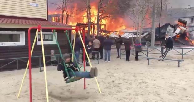 Sudapollismo nivel Dios: Un niño ruso se columpia mientras tiene un enorme incendio detrás