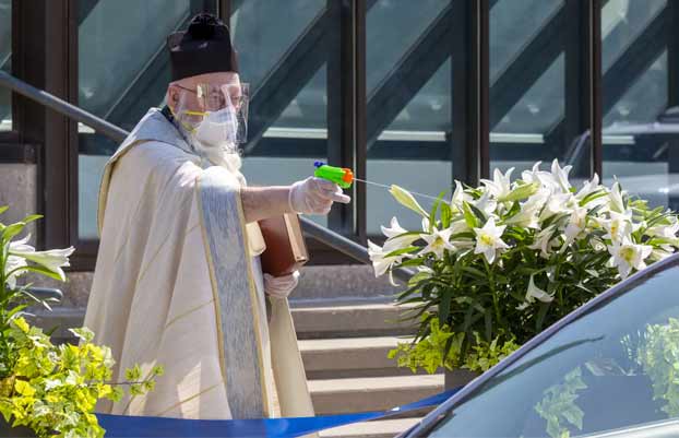 Un sacerdote de Detroit rocía agua bendita con una pistola de agua para mantener el distanciamiento social