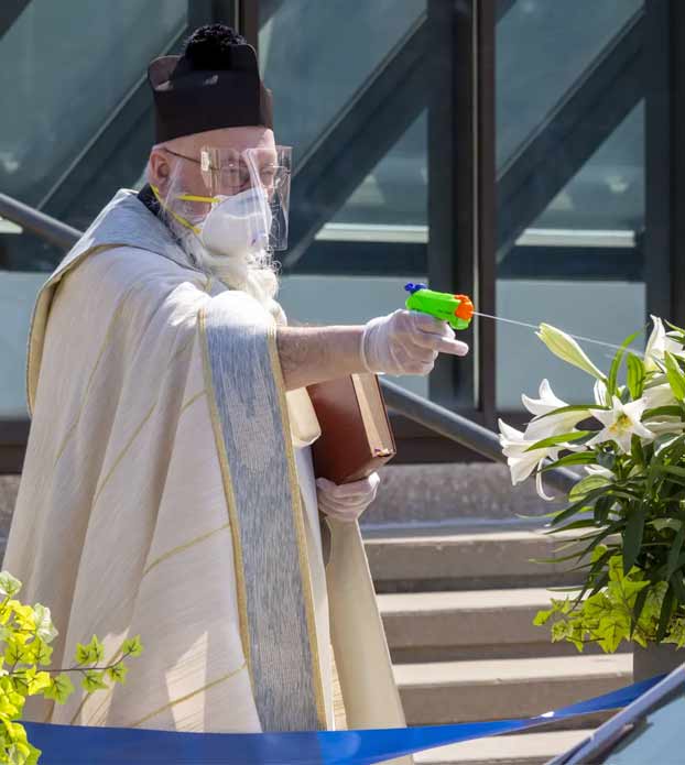 Un sacerdote de Detroit rocía agua bendita con una pistola de agua para mantener el distanciamiento social